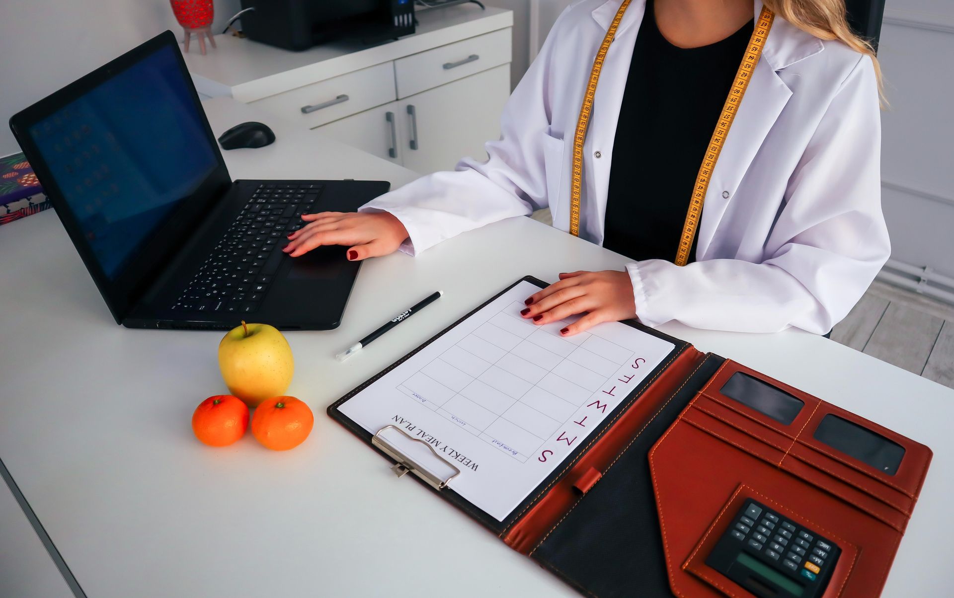 Una mujer está sentada en un escritorio con una computadora portátil y un portapapeles.