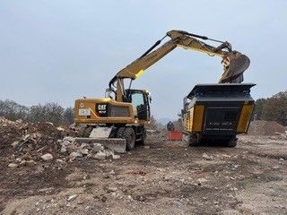 Abrissbagger reißt Gebäude ein – Gelber Bagger im Einsatz bei Abbrucharbeiten, Staub und Trümmer fliegen.