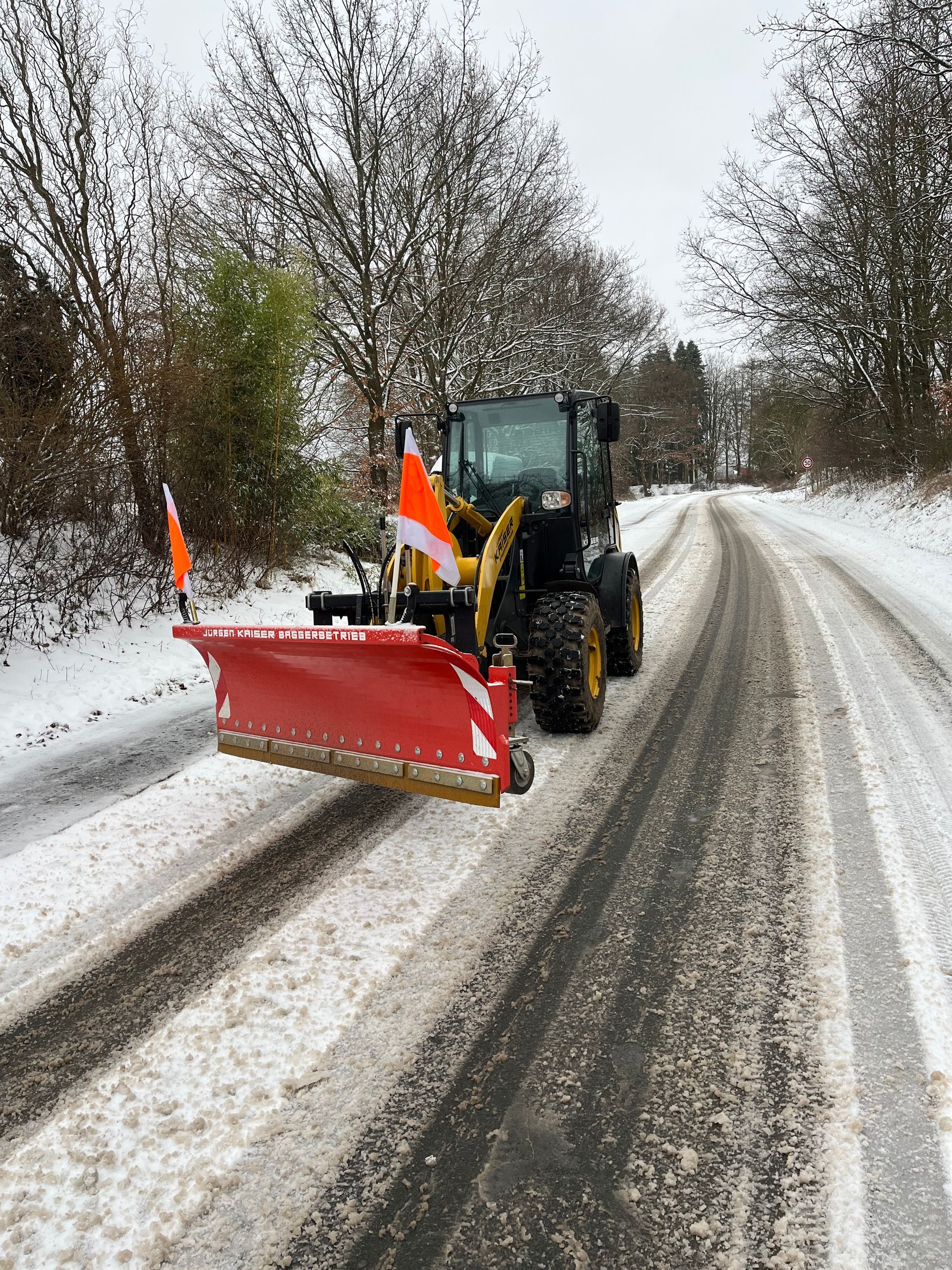Schneepflug im Wintereinsatz – Traktor mit Räumschild und Streuer befreit Straßen von Schnee in verschneiter Stadtlandschaft.