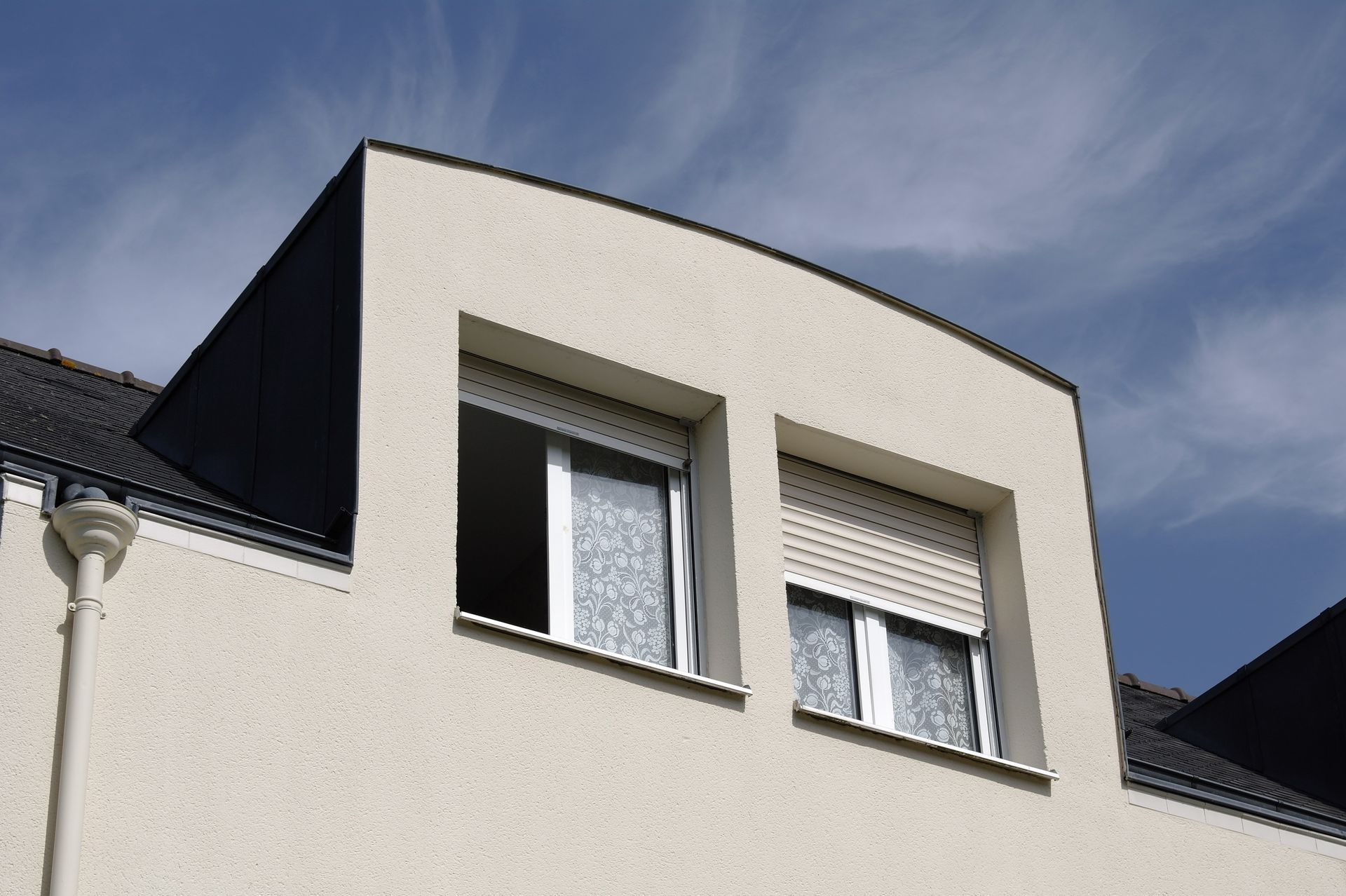 Bâtiment couleur crème avec deux fenêtres et des volets roulants blancs.