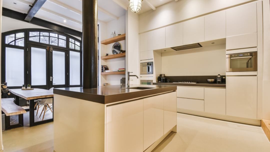 Cocina moderna con isla, gabinetes blancos y gran ventana arqueada.