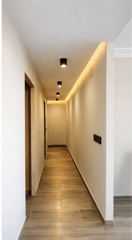 Pasillo largo con piso de madera clara, iluminación empotrada y una tira de luz.