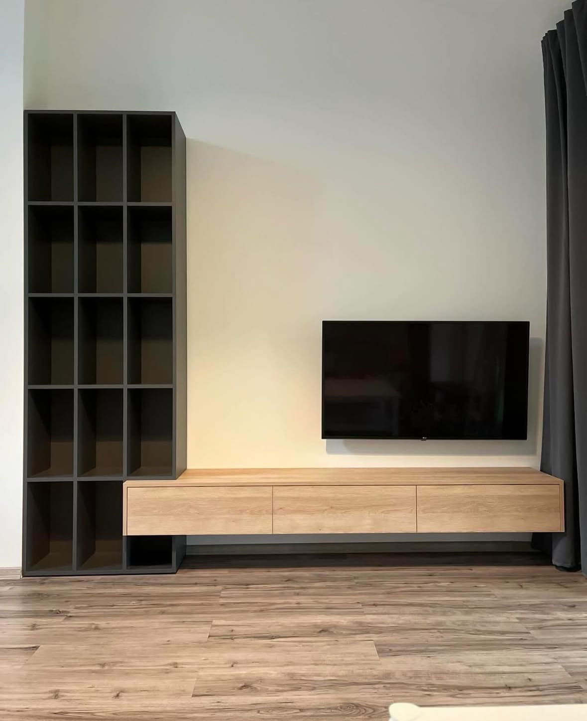 Unidad de entretenimiento moderna con estantes gris oscuro, un mueble flotante de madera clara y un televisor negro.