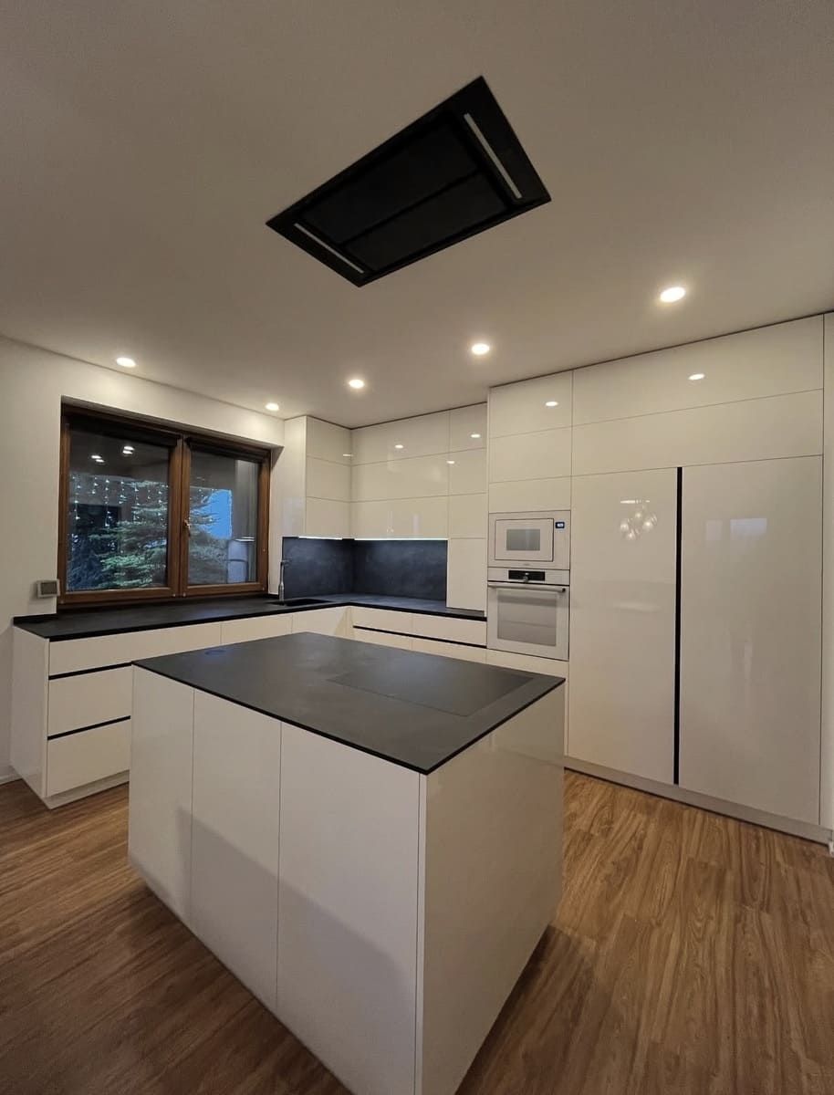 Cocina blanca moderna con isla, encimeras negras, piso de madera y electrodomésticos de acero inoxidable.