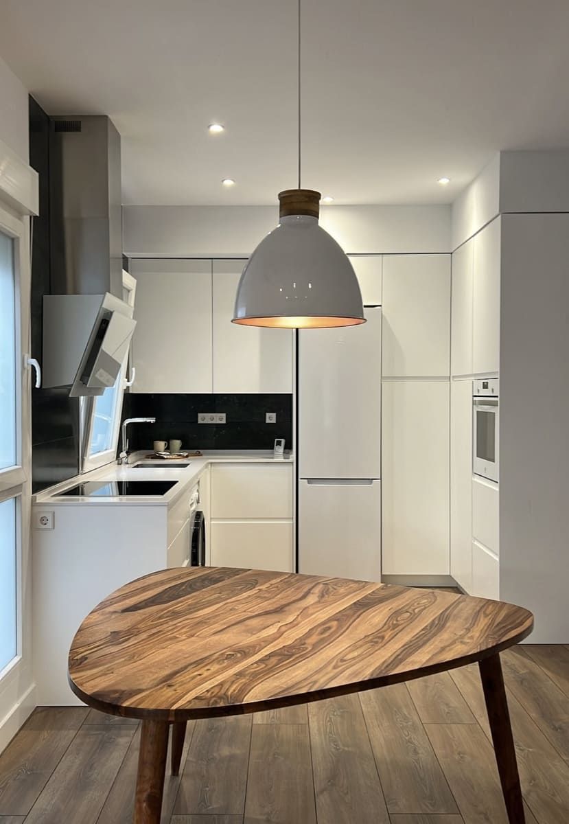 Cocina moderna con gabinetes de madera, isla negra y taburetes. La ventana proporciona luz natural.