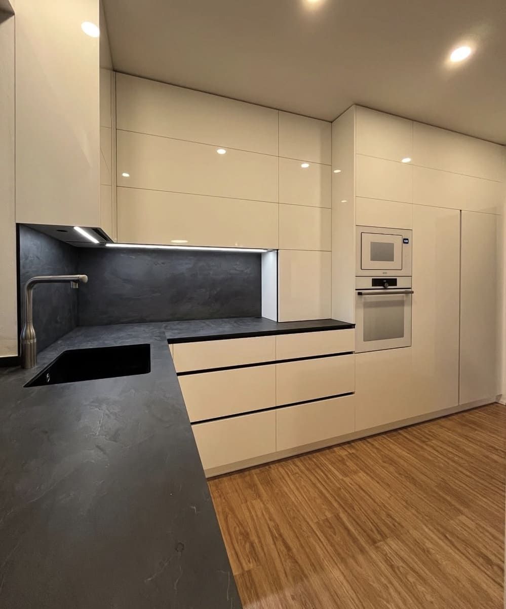 Cocina moderna con gabinetes blancos, encimera oscura y electrodomésticos empotrados.