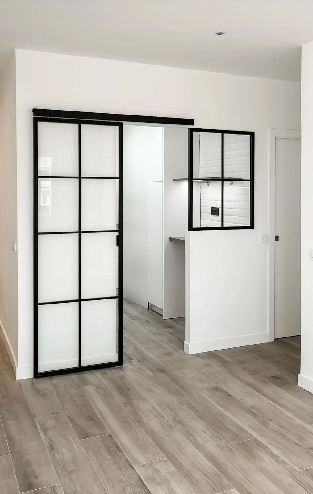 Puerta corrediza de vidrio con marco negro con una ventana a juego en una habitación blanca con piso de madera.