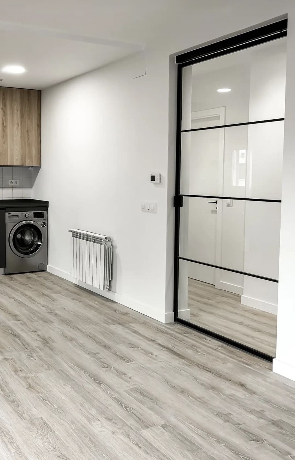 Fotografía interior de una cocina moderna con lavadora, gabinetes de madera y una puerta de vidrio con molduras negras.