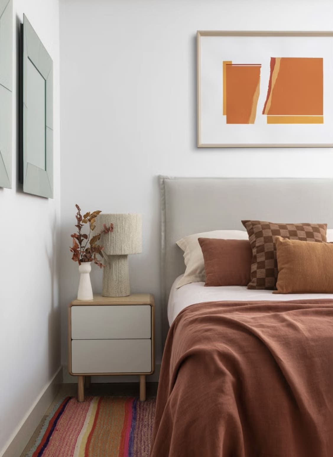 Acogedor dormitorio con ropa de cama de color óxido, obras de arte y una mesita de noche con lámpara.