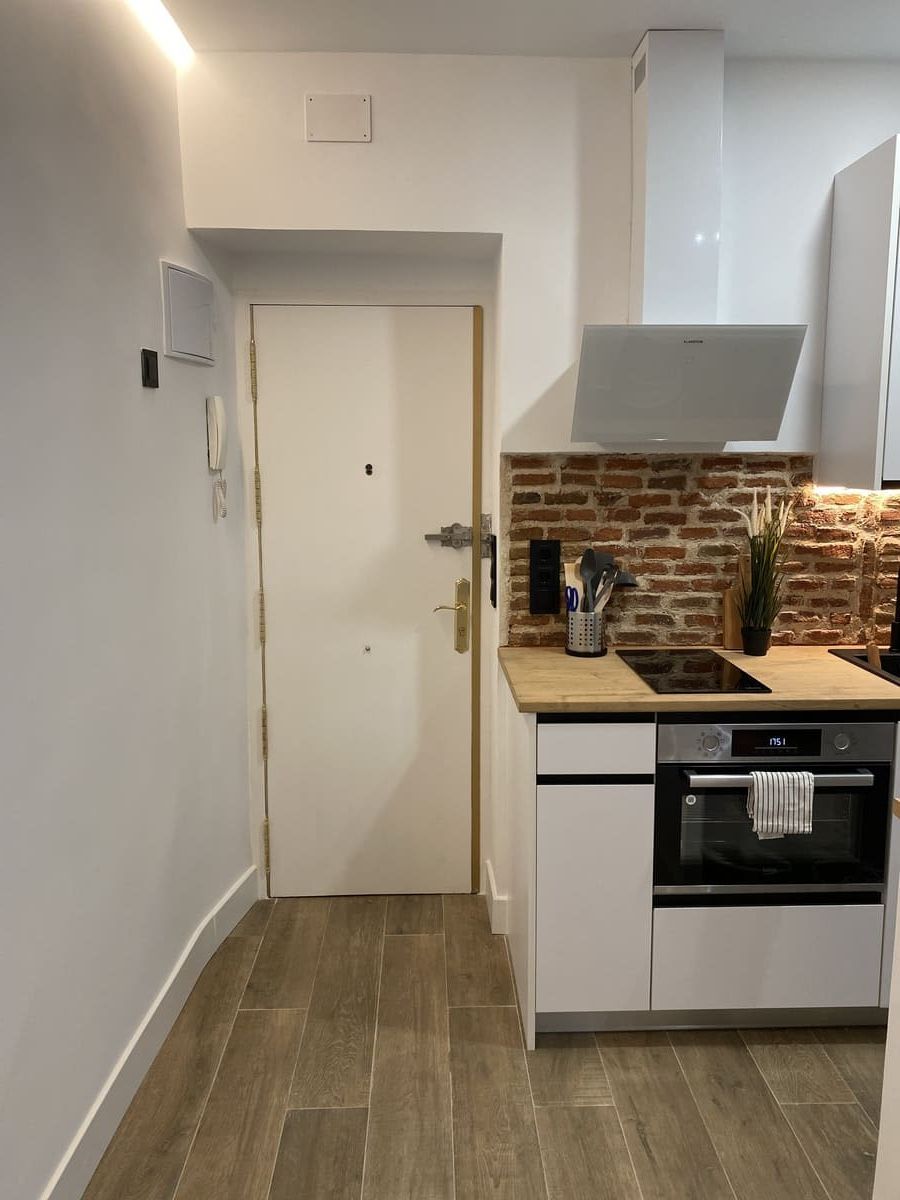 Pequeña cocina blanca con encimera de madera, salpicadero de ladrillo y puerta.