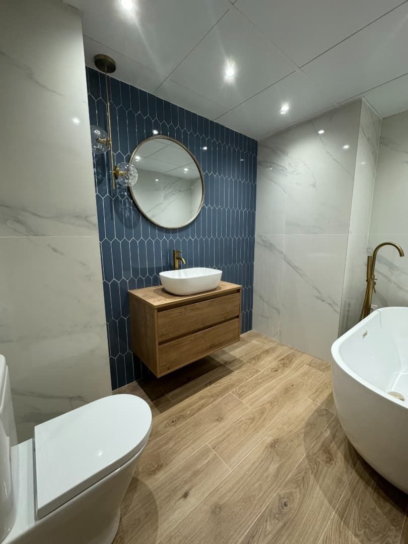 Baño moderno con pared decorativa de azulejos azules, tocador de madera, espejo redondo y bañera blanca.