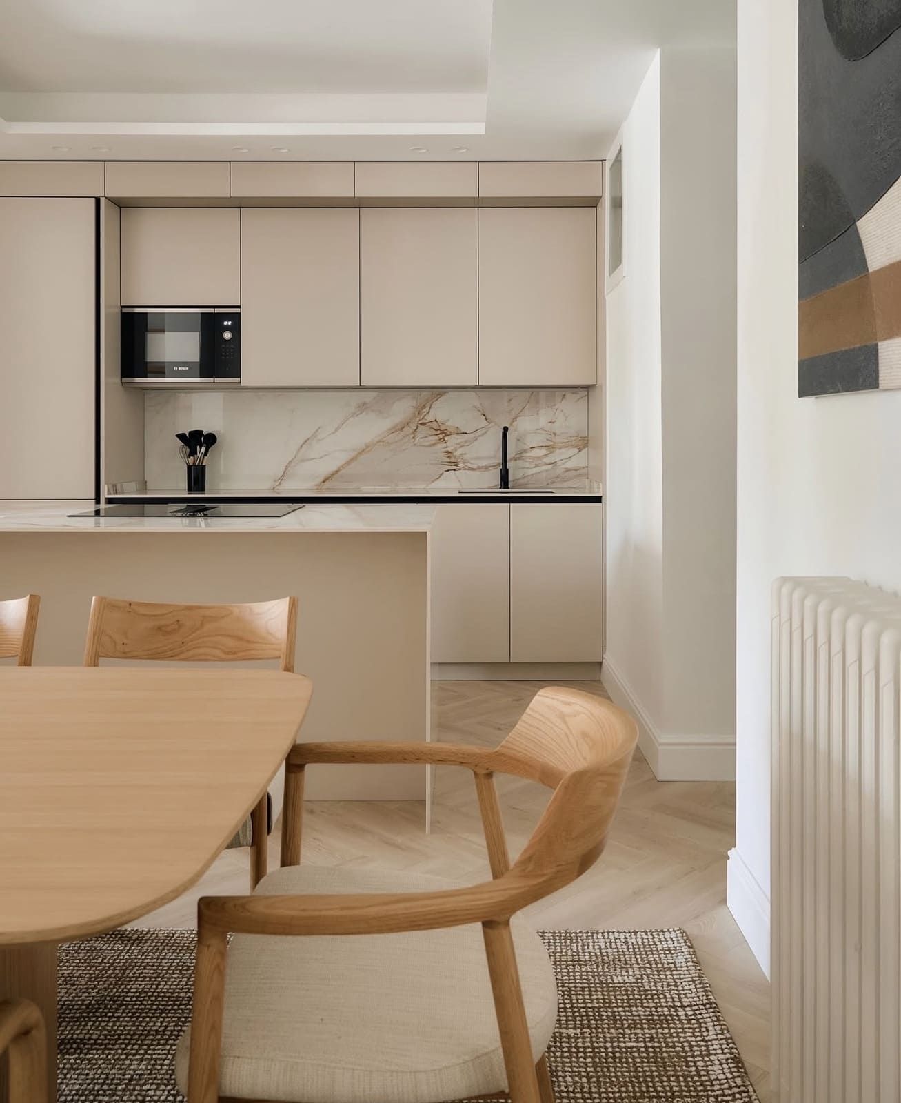 Cocina moderna con gabinetes beige, salpicadero de mármol y mesa de comedor de madera.