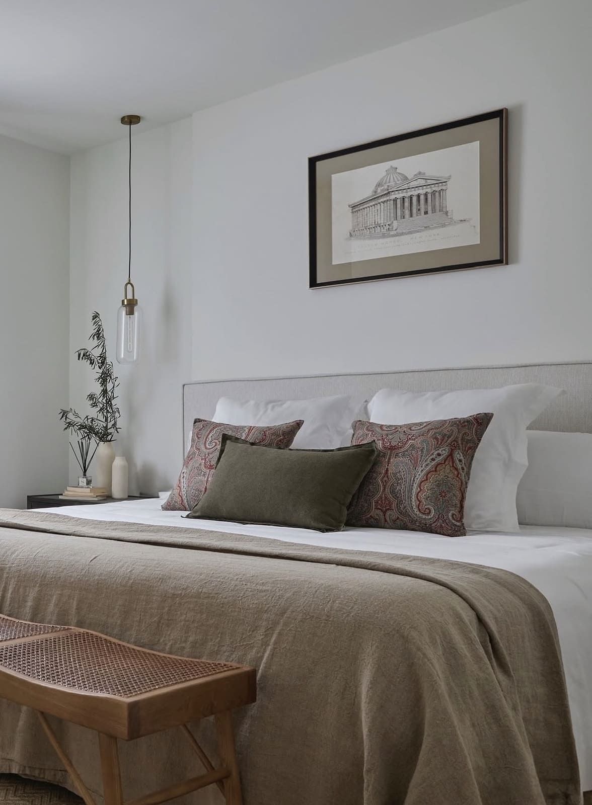 Dormitorio con cama blanca, manta beige y lámina arquitectónica enmarcada.