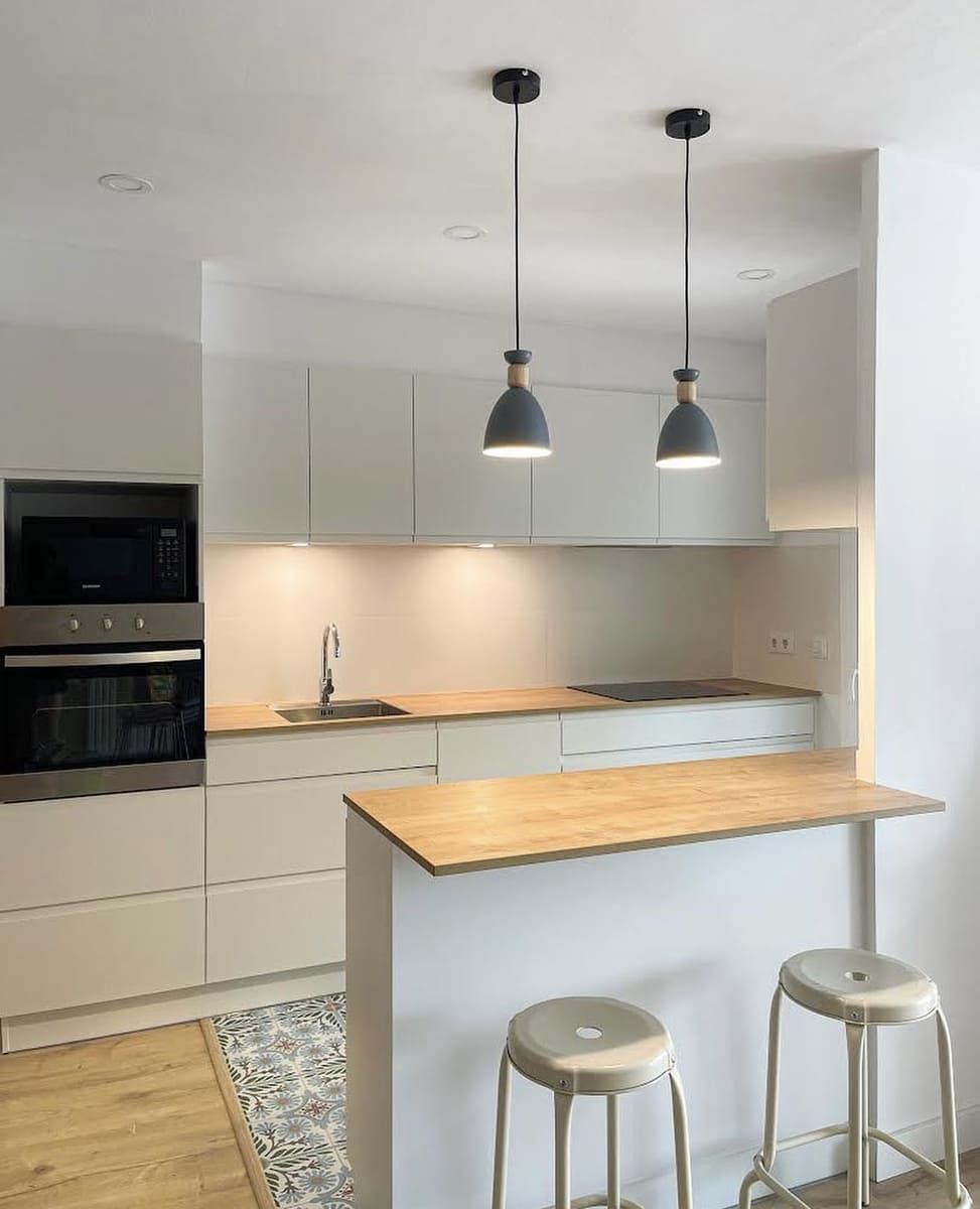 Cocina moderna con gabinetes blancos, encimeras de madera y dos luces colgantes.