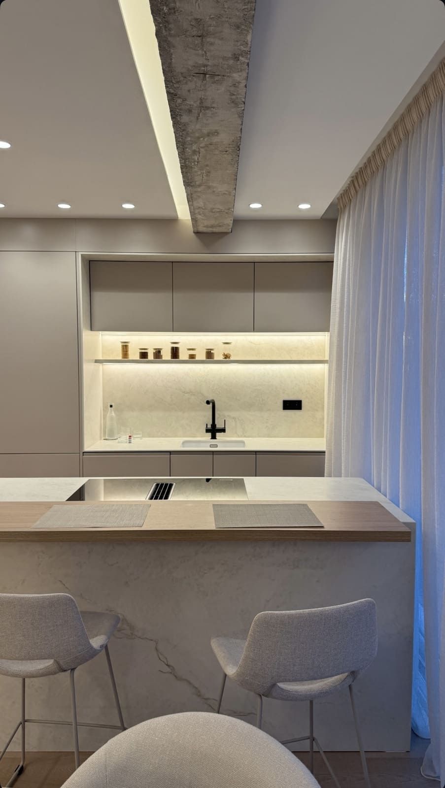 Cocina moderna con tonos neutros claros, asientos de barra y vigas de techo texturizadas.