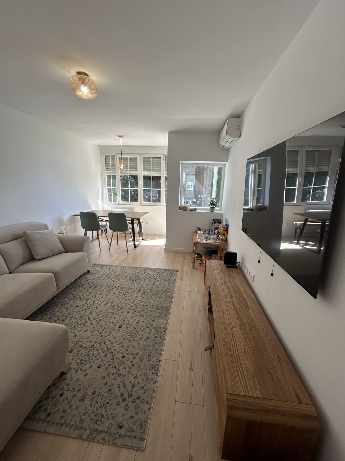 Sala de estar con sofá, alfombra, comedor y TV de pared.