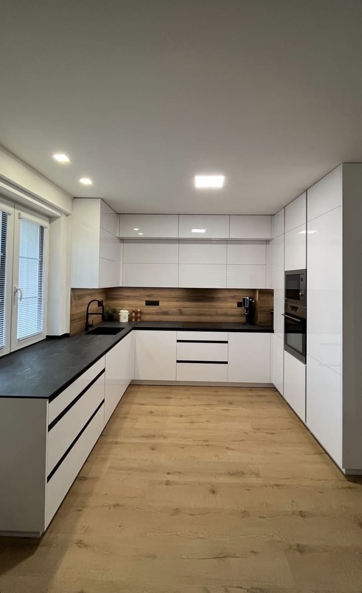 Cocina blanca moderna con salpicadero de madera y encimeras negras.