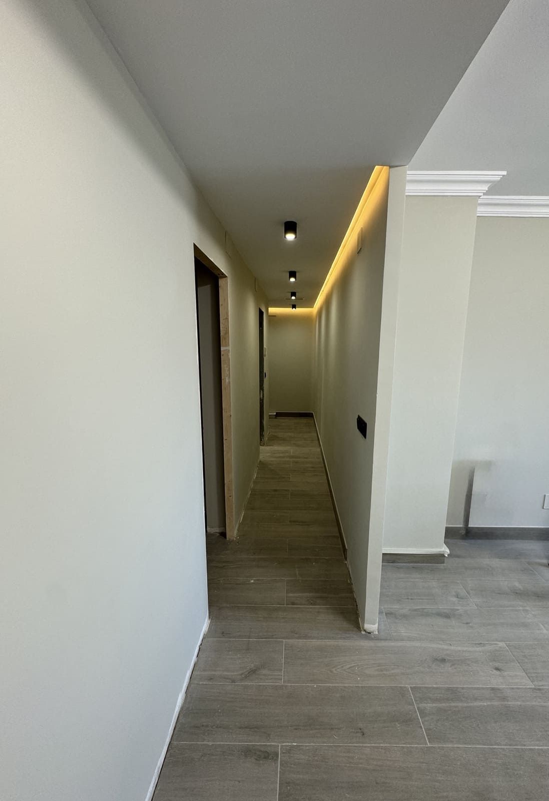 Pasillo largo con suelo de baldosas grises, puertas e iluminación empotrada en el techo.