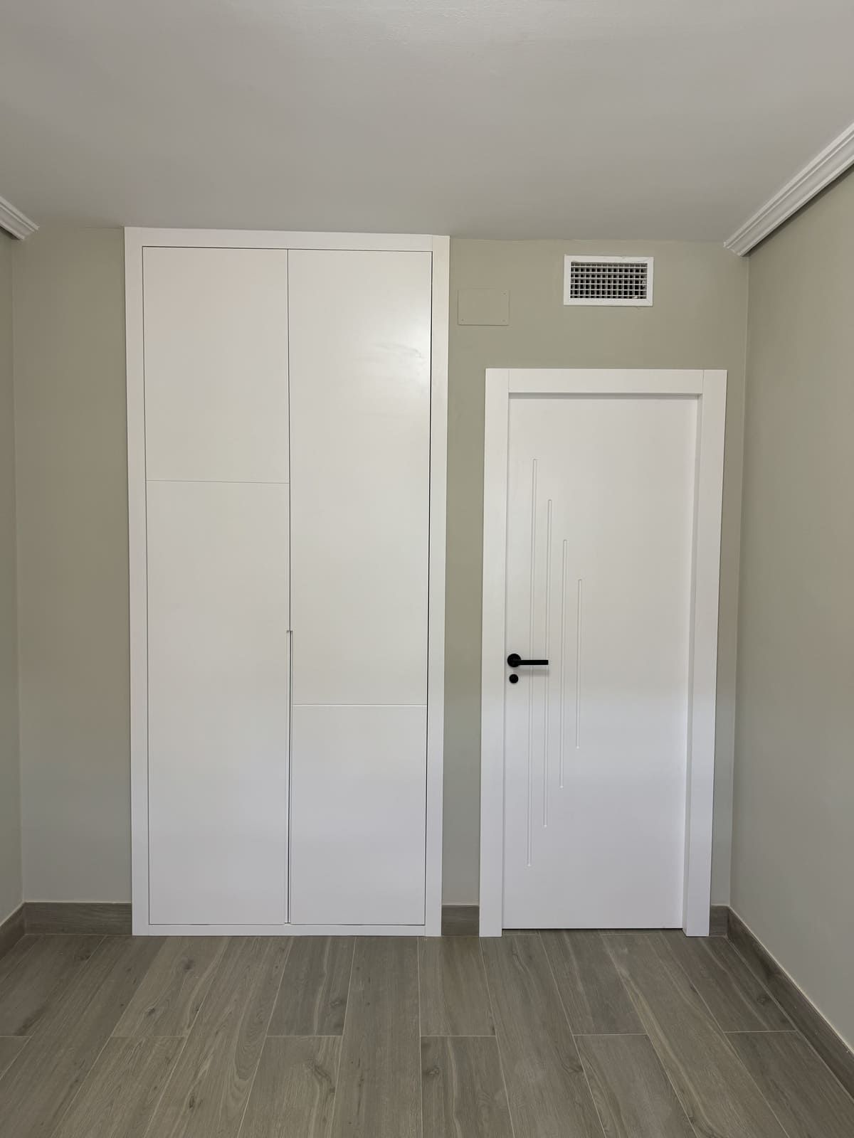 Armario y puerta blancos contra una pared gris pálido, habitación con suelo imitación madera.