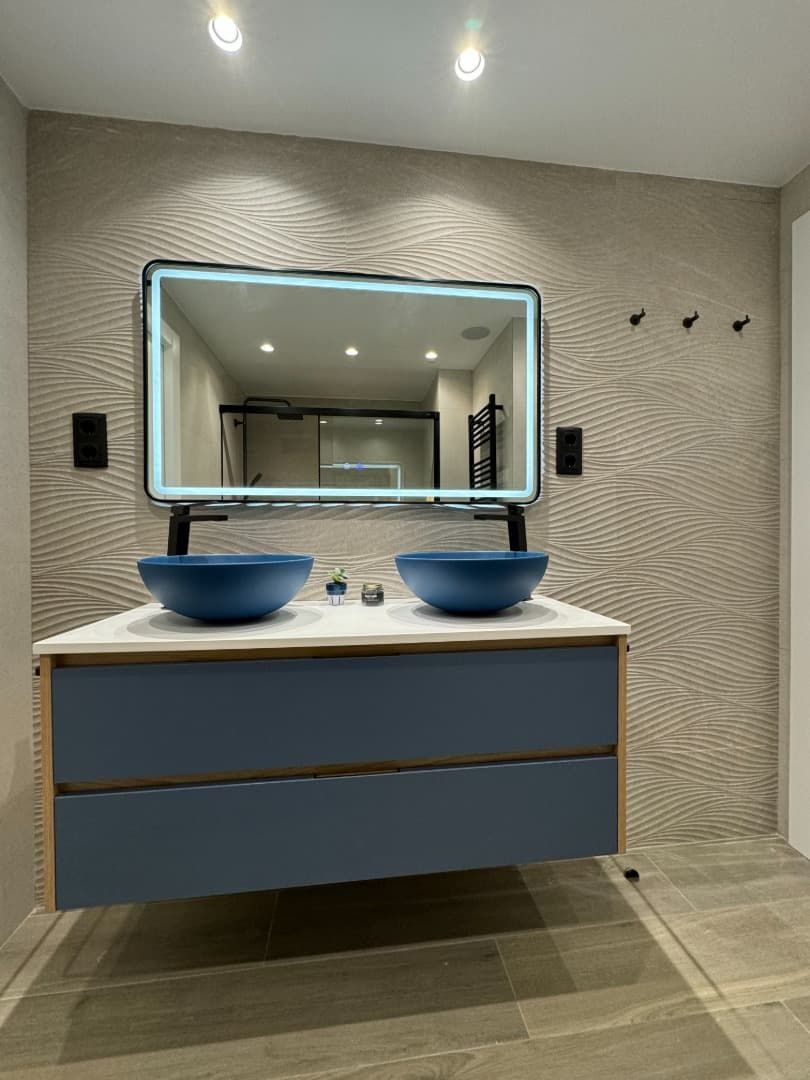 Baño moderno con tocador flotante azul, lavabos tipo vasija y espejo iluminado.