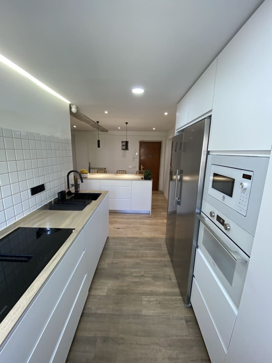 Cocina moderna con muebles blancos y de madera, isla con taburetes y lámparas colgantes. Etiqueta 