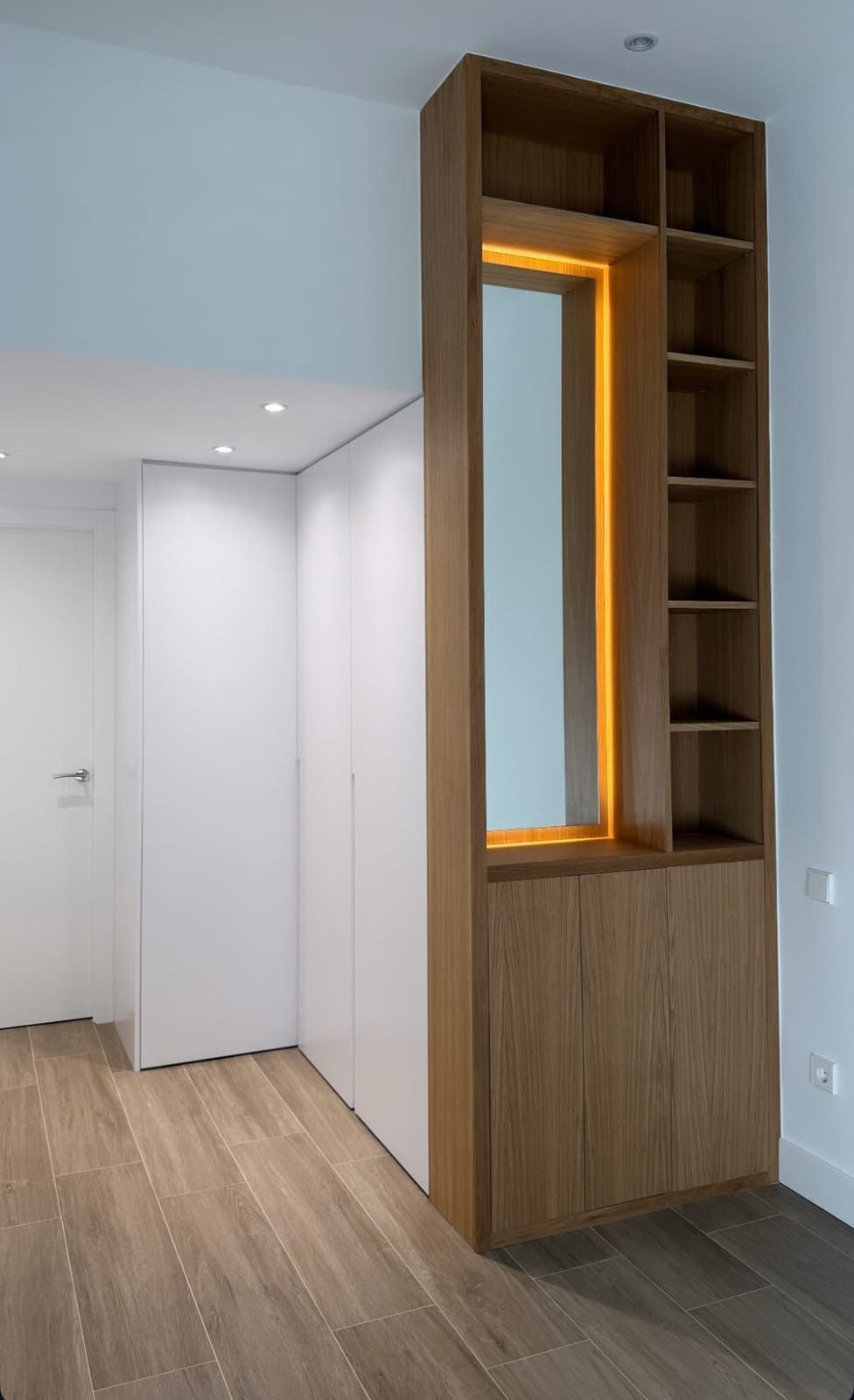 Mueble de madera con espejo y estantes en una habitación con paredes blancas y suelo de madera.