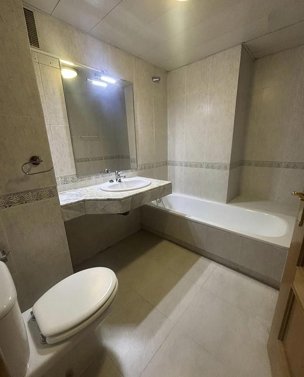 Baño con diseño de azulejos azules y blancos, tocador de madera, inodoro y bañera.