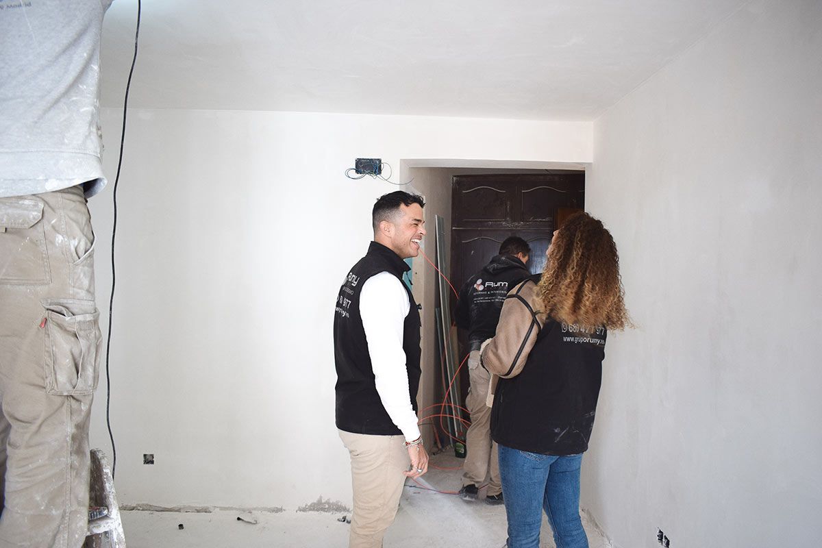 Sala de estar bohemia con pared de acento verde, sofá, muebles de ratán y alfombra redonda.