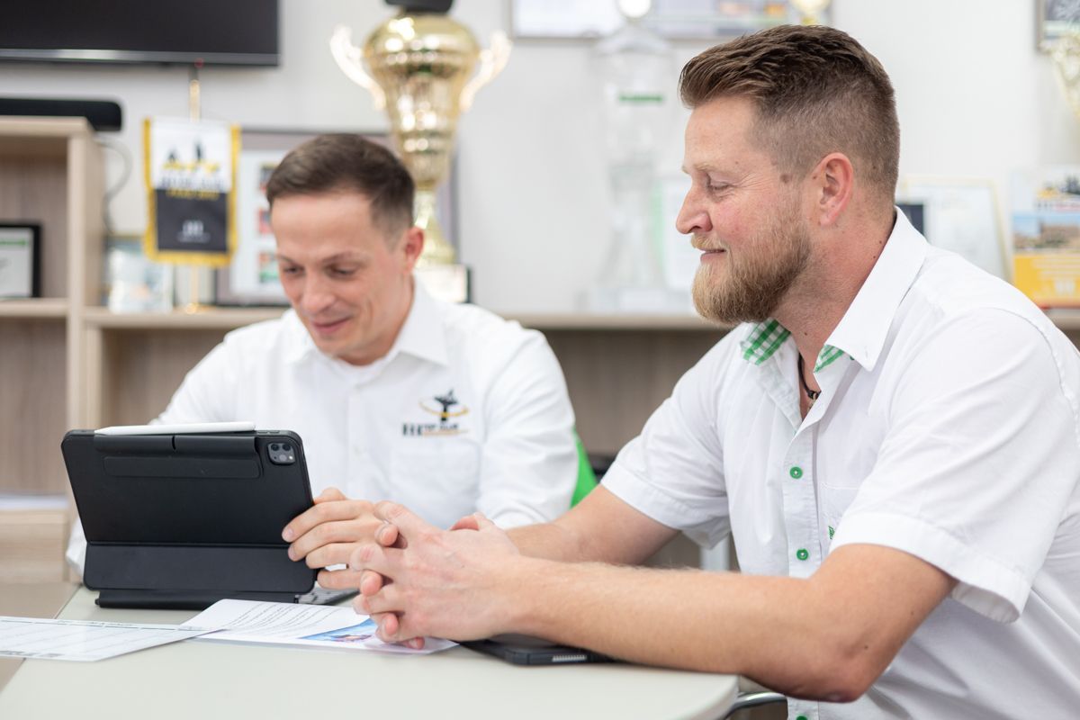 Zwei Männer sitzen an einem Tisch und schauen auf einen Tablet-Computer.