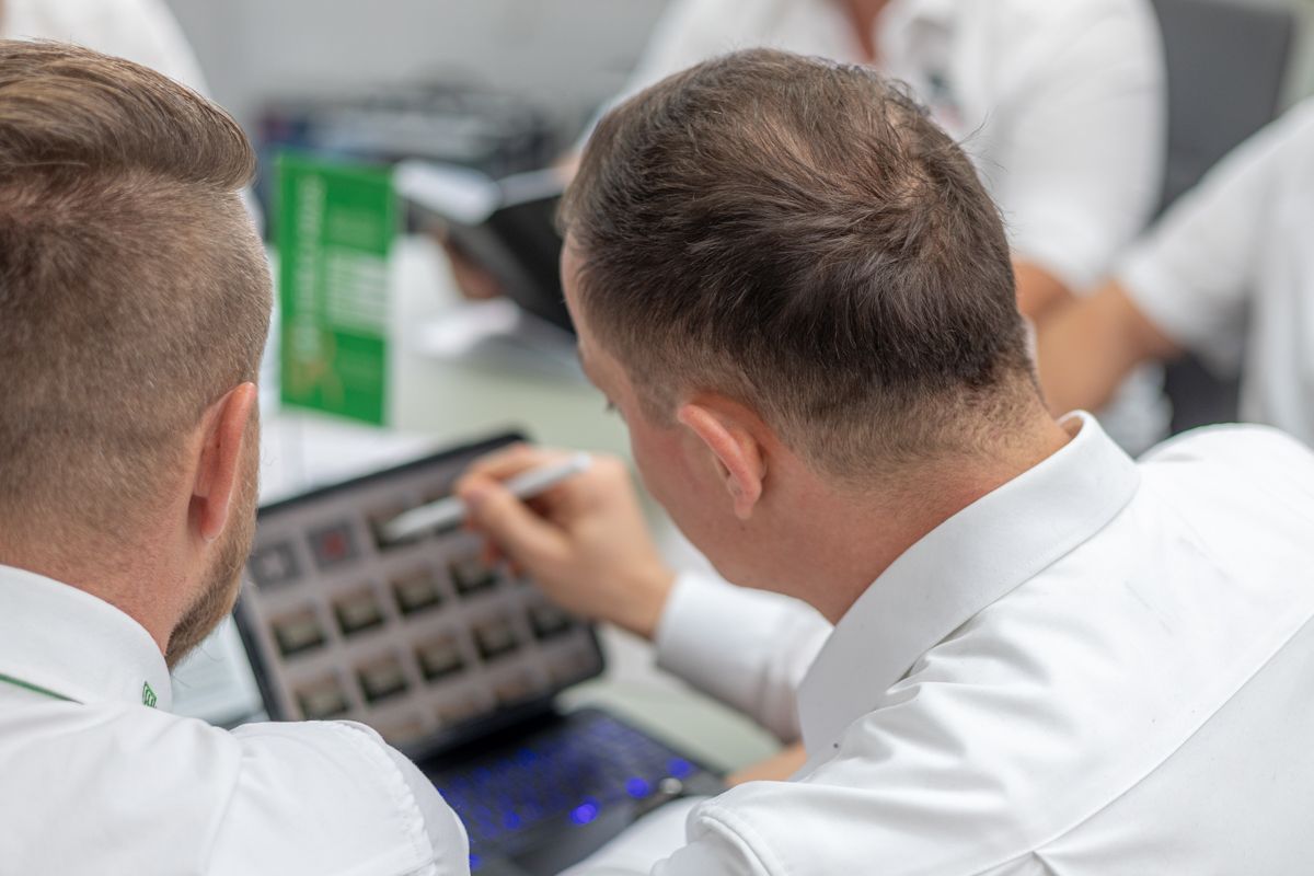 Zwei Männer sitzen an einem Tisch und schauen auf einen Laptop.