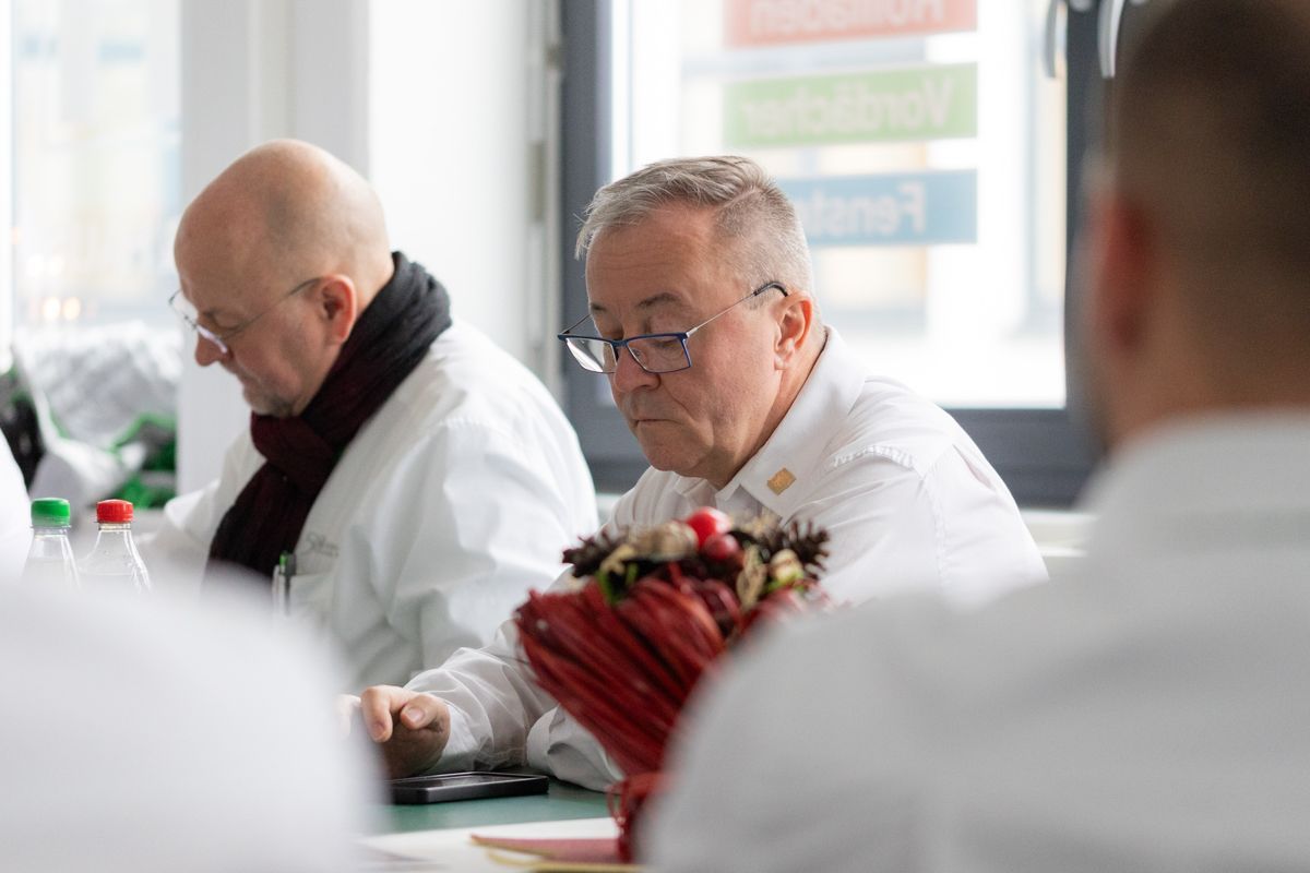 Eine Gruppe Männer sitzt an einem Tisch vor einem Fenster.