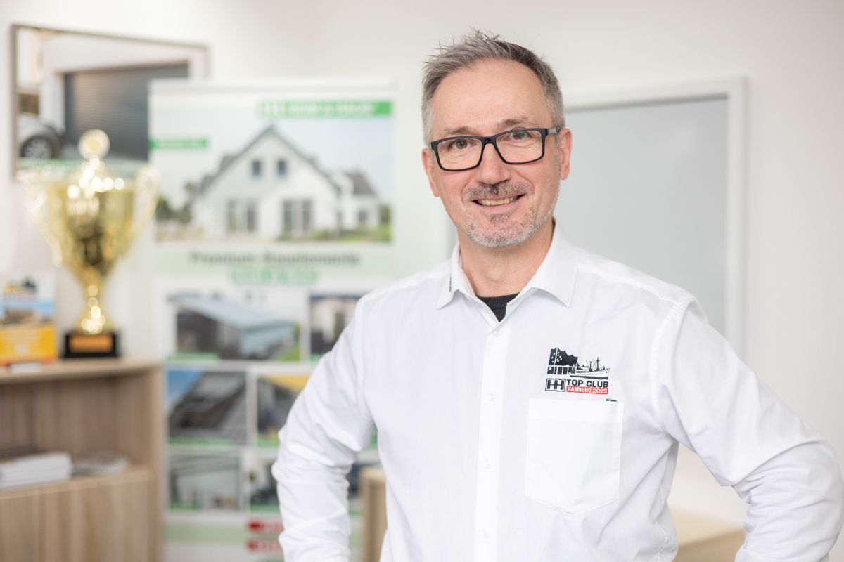 Ein Mann mit Brille und weißem Hemd steht vor einer Trophäe.