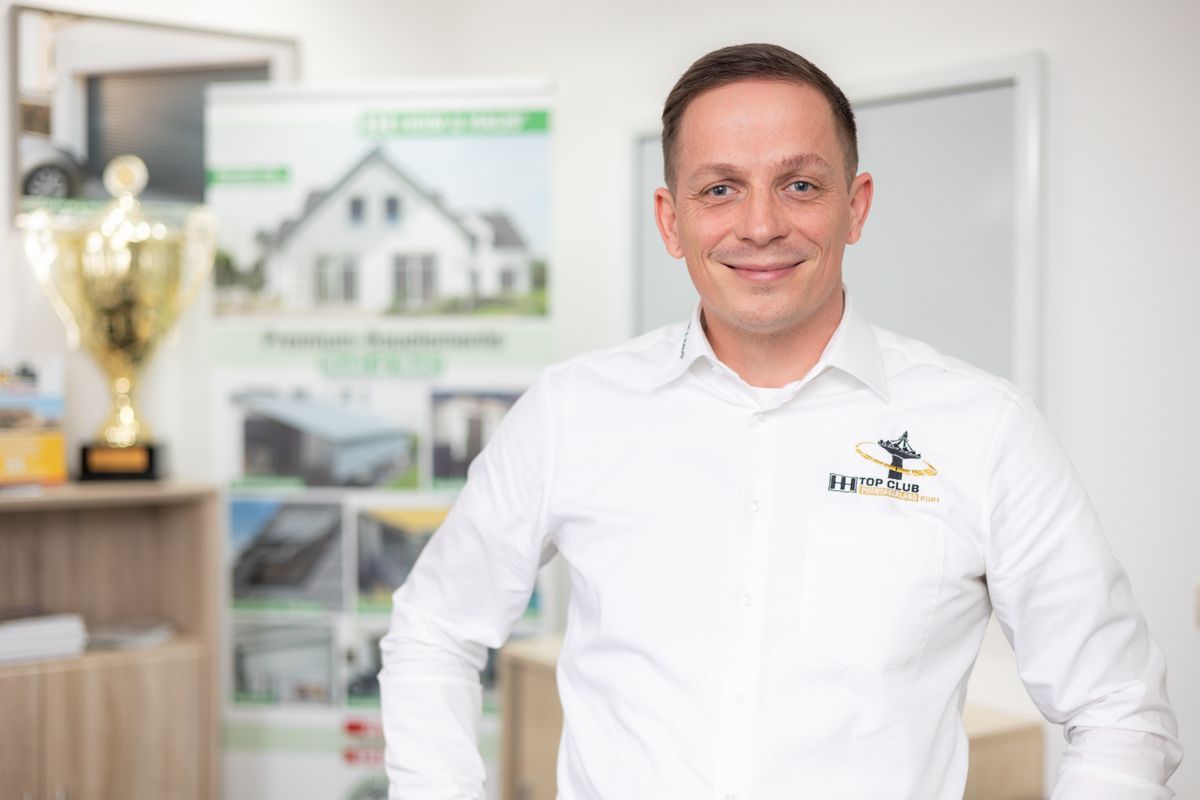 Ein Mann in einem weißen Hemd steht vor einem Schild.