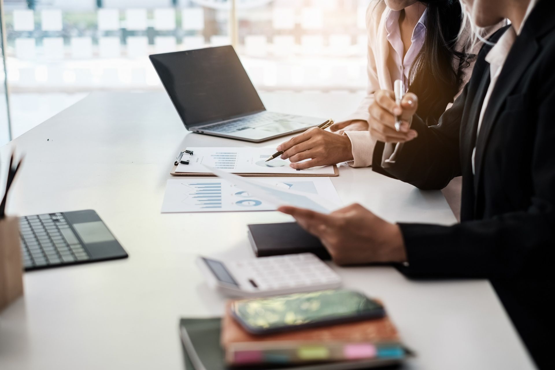Dos personas de negocios en un escritorio revisando informes financieros con una computadora portátil y una calculadora.