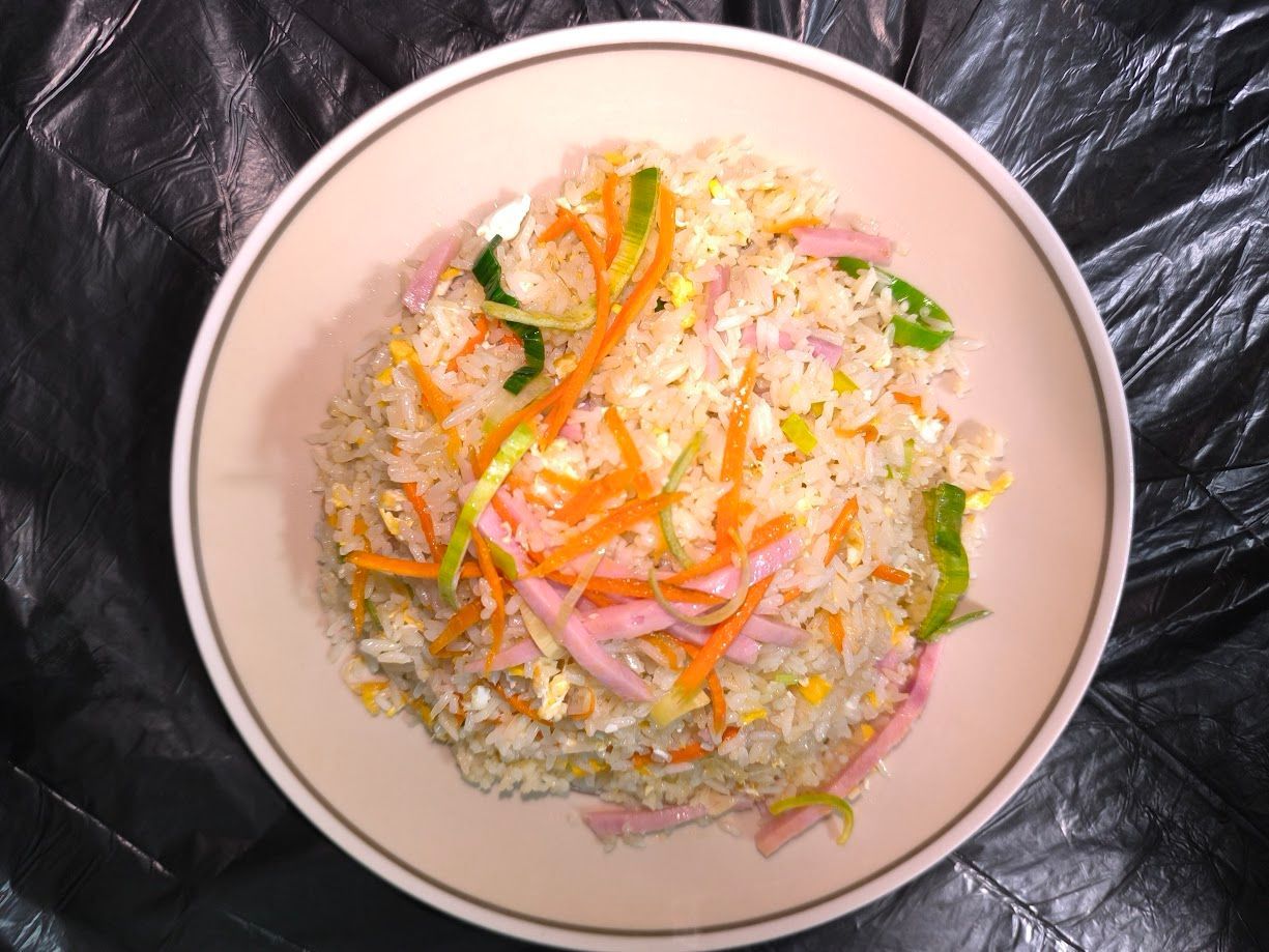 Arroz frito con tiras de zanahoria y cebolla en un recipiente blanco, sobre un fondo negro.