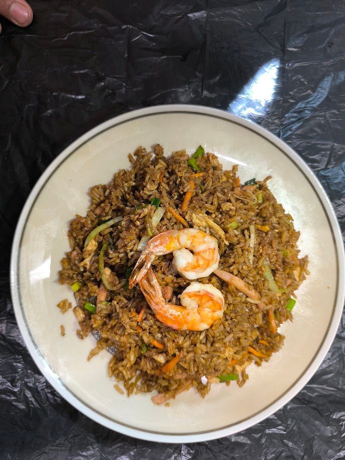 Arroz frito con camarones en un plato blanco, con dos camarones cocidos encima. Contiene zanahoria, cebolla y semillas de sésamo.