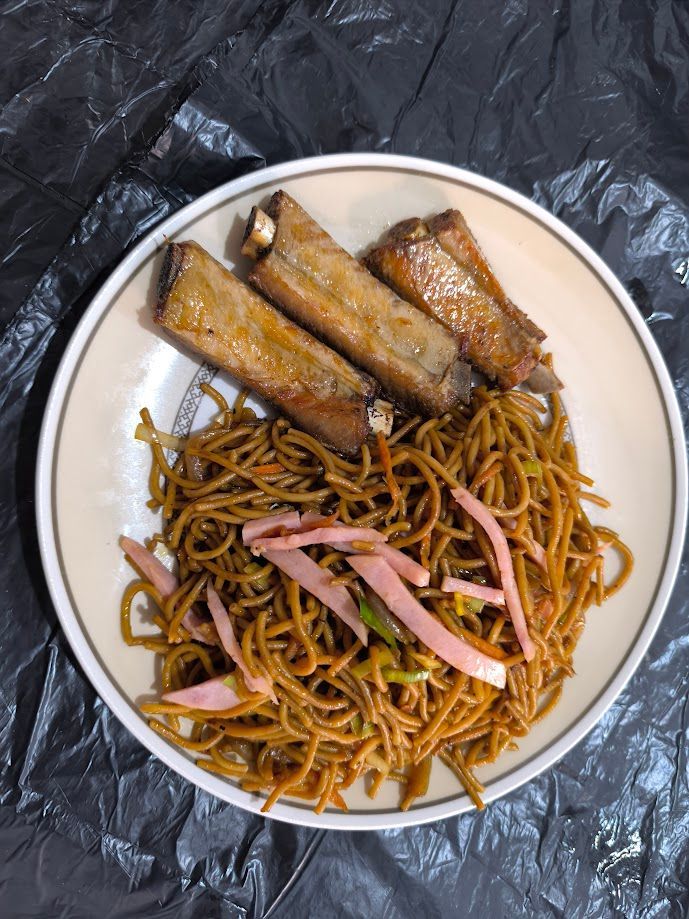 Plato con fideos y costillas glaseadas, adornado con jengibre encurtido rosado, sobre una superficie negra.