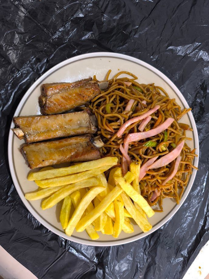 Plato de comida con costillas, fideos y papas fritas. Las costillas están glaseadas, los fideos están dorados y las papas fritas, también.