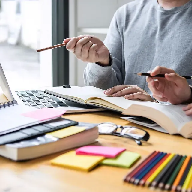 Dos personas están sentadas en un escritorio con libros y una computadora portátil.