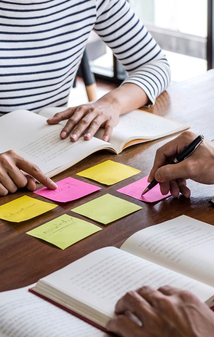 Dos personas están sentadas en una mesa leyendo libros y escribiendo en notas adhesivas.