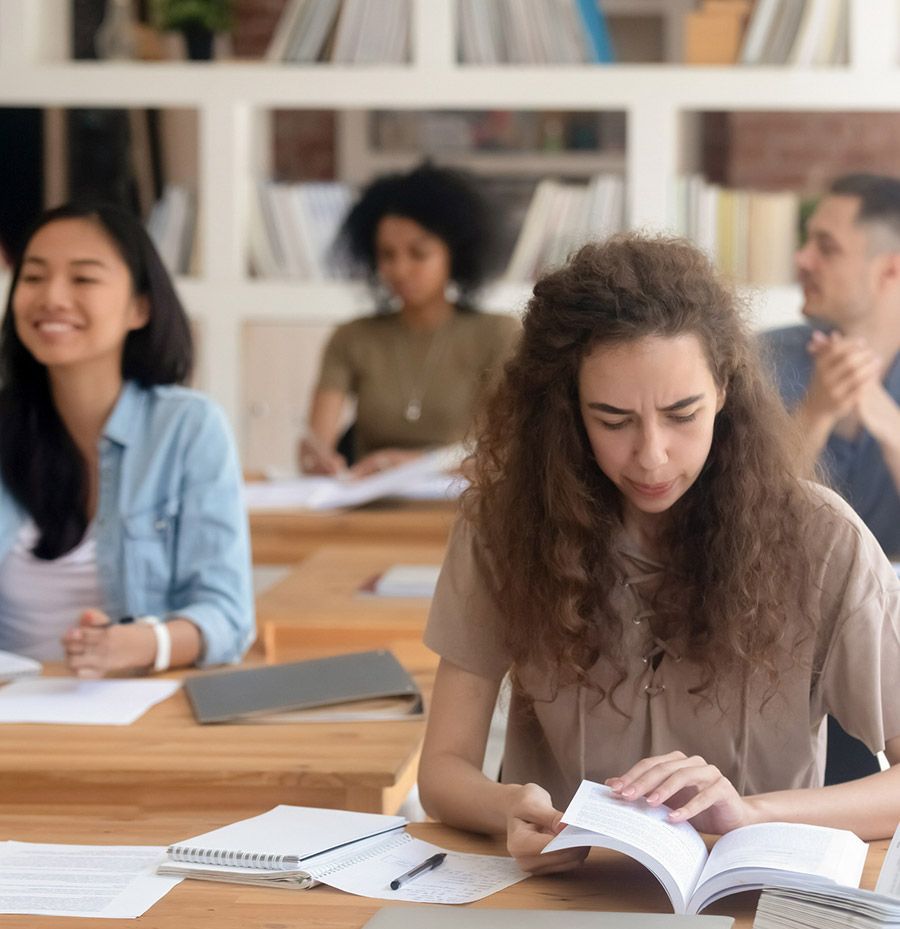 Un grupo de personas están sentadas en escritorios en un aula leyendo libros.