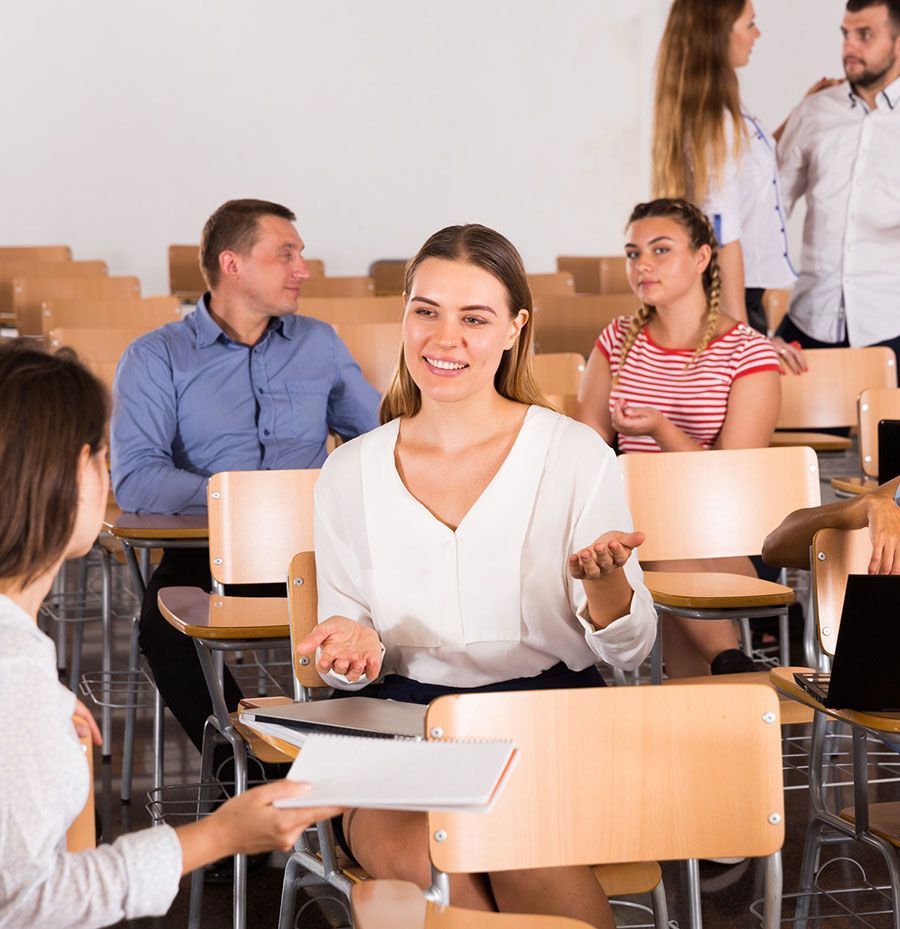 Un grupo de personas están sentadas en escritorios en un aula hablando entre sí.