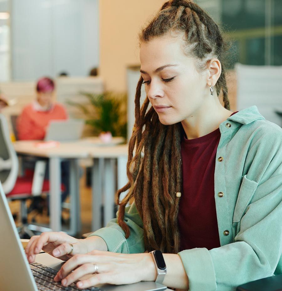 Una mujer con rastas está escribiendo en una computadora portátil.