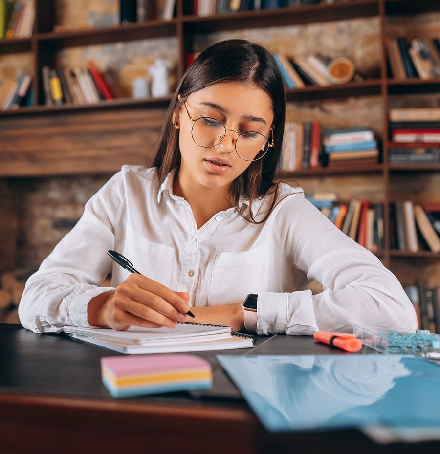 Una mujer está sentada en un escritorio escribiendo en un cuaderno.