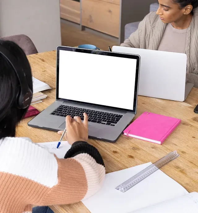 Dos mujeres están sentadas en una mesa utilizando computadoras portátiles.