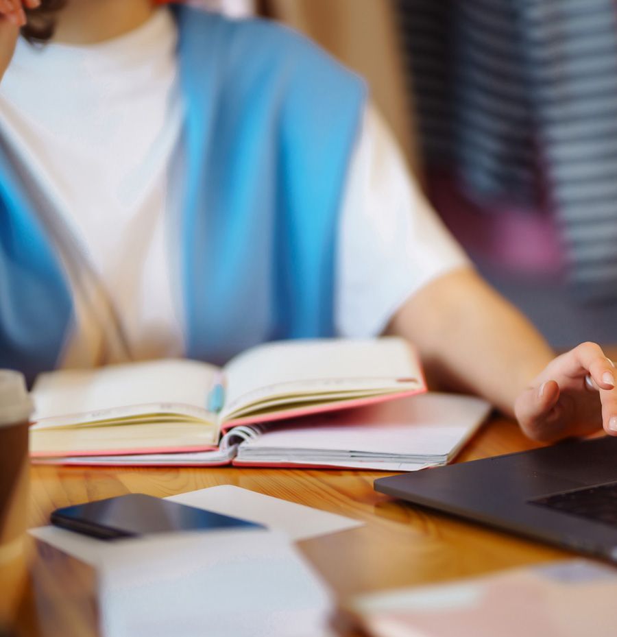 Una mujer está sentada en una mesa con una computadora portátil y un libro.