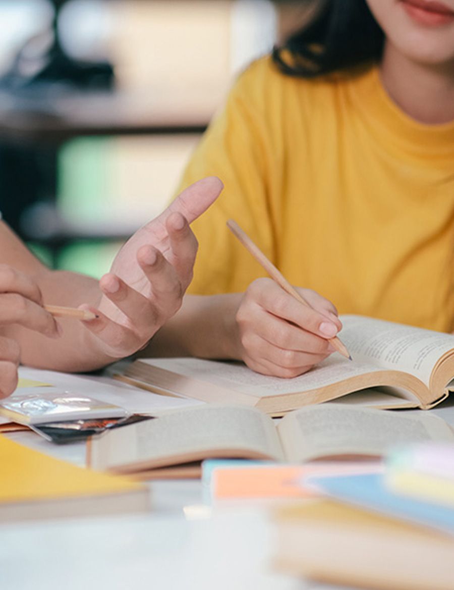 Una mujer con una camisa amarilla está sentada en una mesa con un libro y un bolígrafo.
