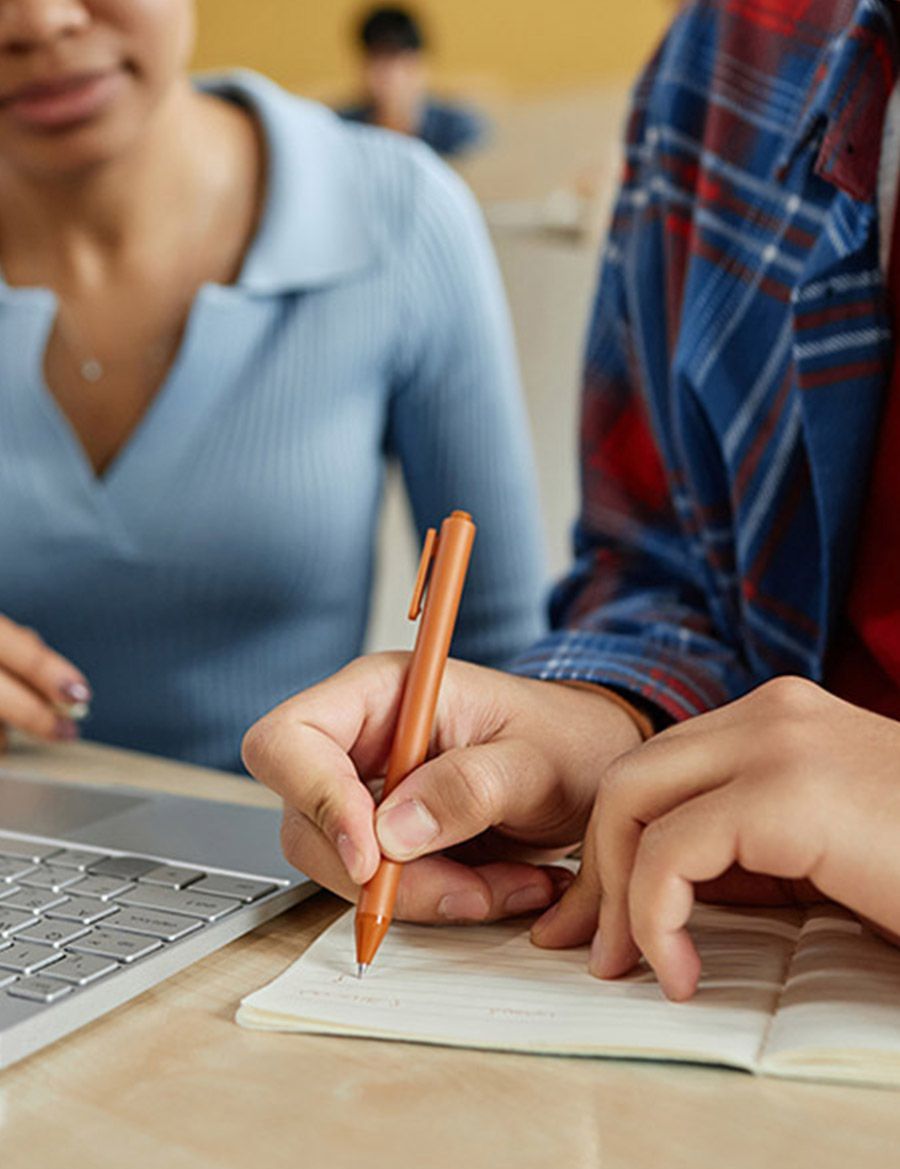Una persona está escribiendo en un cuaderno junto a una computadora portátil.