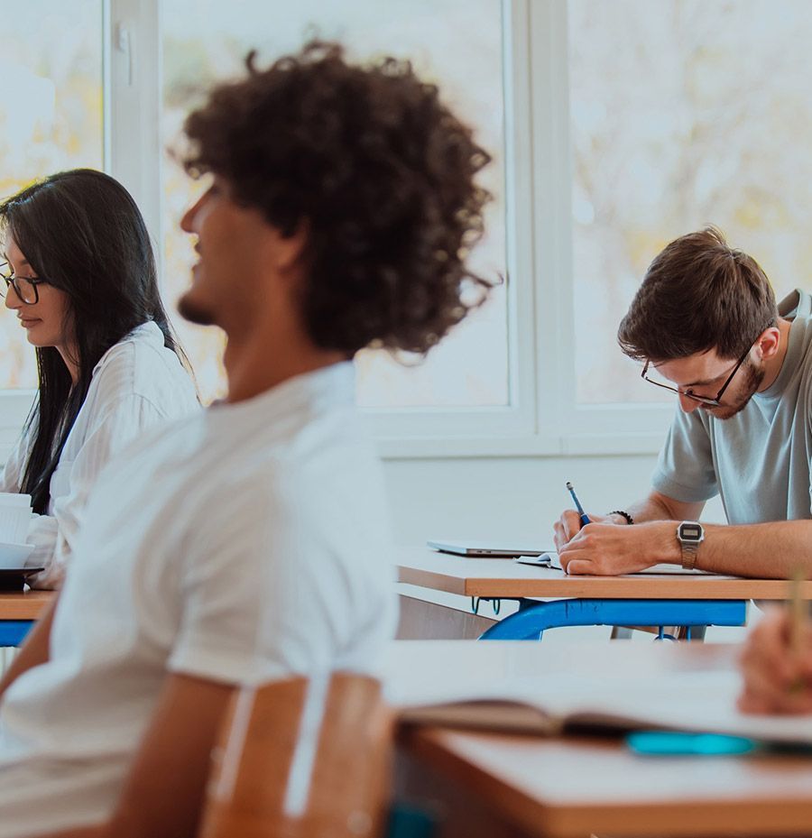 Un grupo de personas están sentadas en escritorios en un aula.