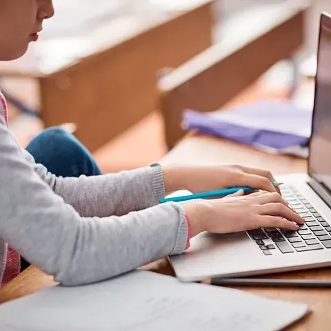 Una niña está escribiendo en una computadora portátil.
